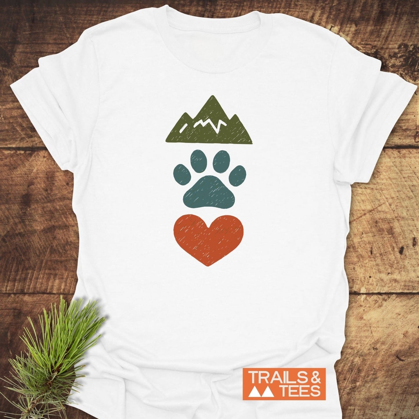 Mountains & Dogs Love T-Shirt featuring mountain, paw, and heart icons. Soft, durable, pre-shrunk cotton for outdoor enthusiasts. Overlapping TRAILS & TEES logo.