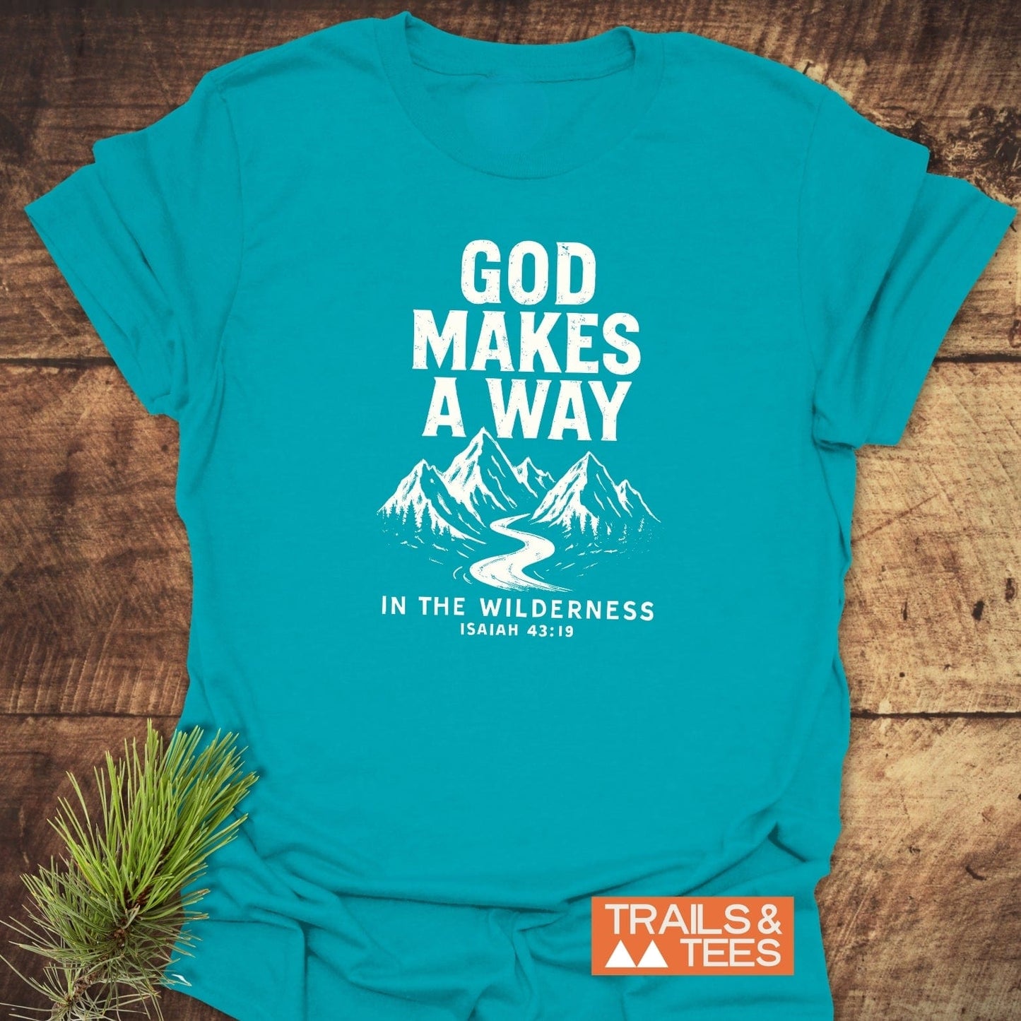 Turquoise God Makes A Way T-shirt with mountain and river design, laid on wood; features comfort-fit, durable print, made for outdoor enthusiasts by Trails & Tees.