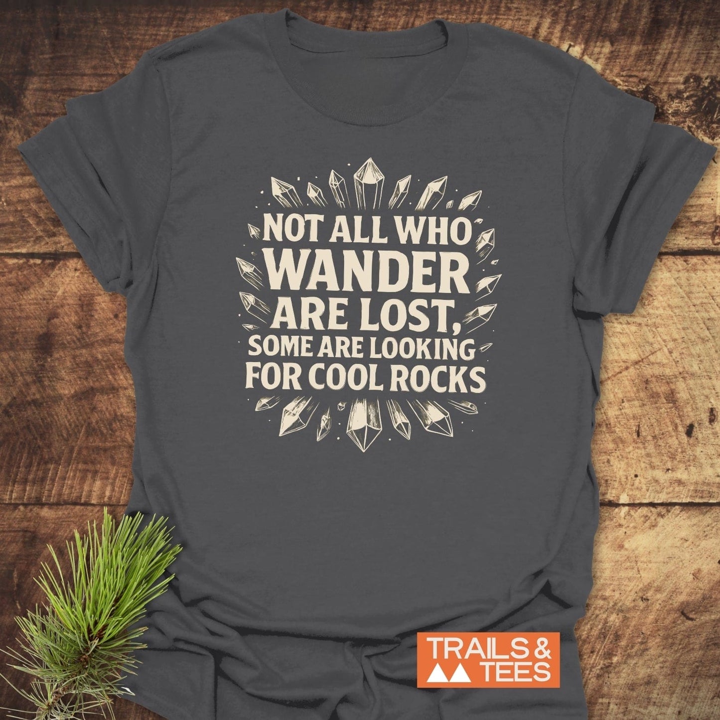 Dark-gray 764 Not All... Rock Lover T-Shirt with white crystal graphic and quote, laid on wooden surface, featuring Trails & Tees logo.