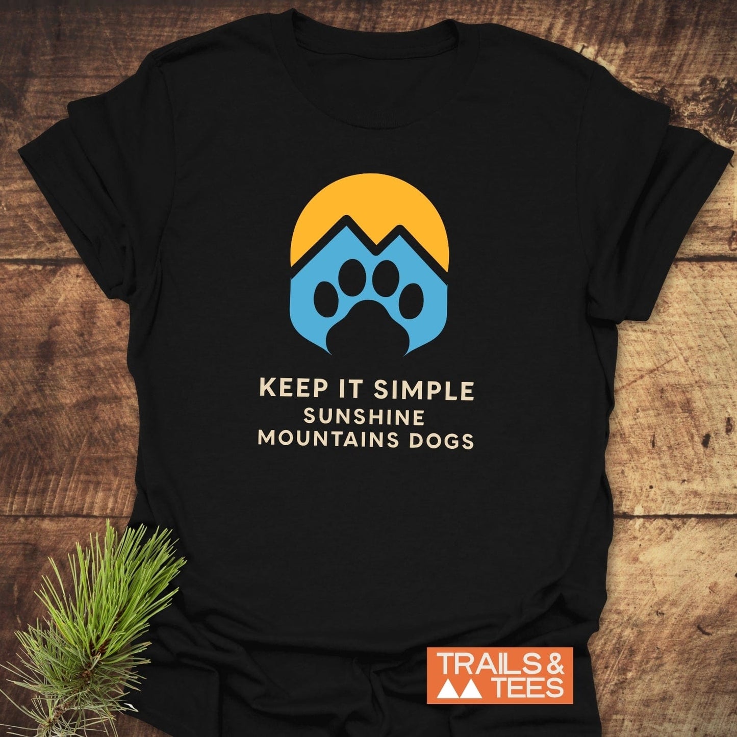 Sun Mountains Dogs T-Shirt on rustic wood, featuring a sun, mountain peaks, and paw print graphic. Text reads: KEEP IT SIMPLE SUNSHINE MOUNTAINS DOGS.