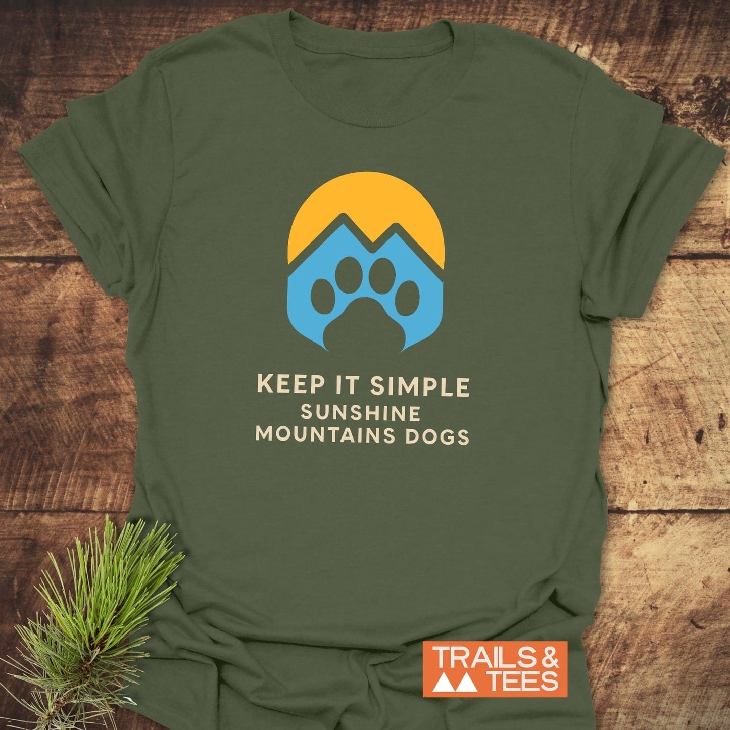 Sun Mountains Dogs T-Shirt on a rustic surface, featuring a sun and mountain paw print design, with the slogan KEEP IT SIMPLE SUNSHINE MOUNTAINS DOGS.