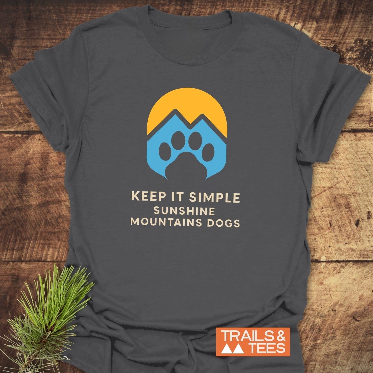 Sun Mountains Dogs T-Shirt on rustic wood, featuring a yellow sun over blue peaks and paw, with slogan. Soft, durable, pre-shrunk cotton for outdoor lovers.