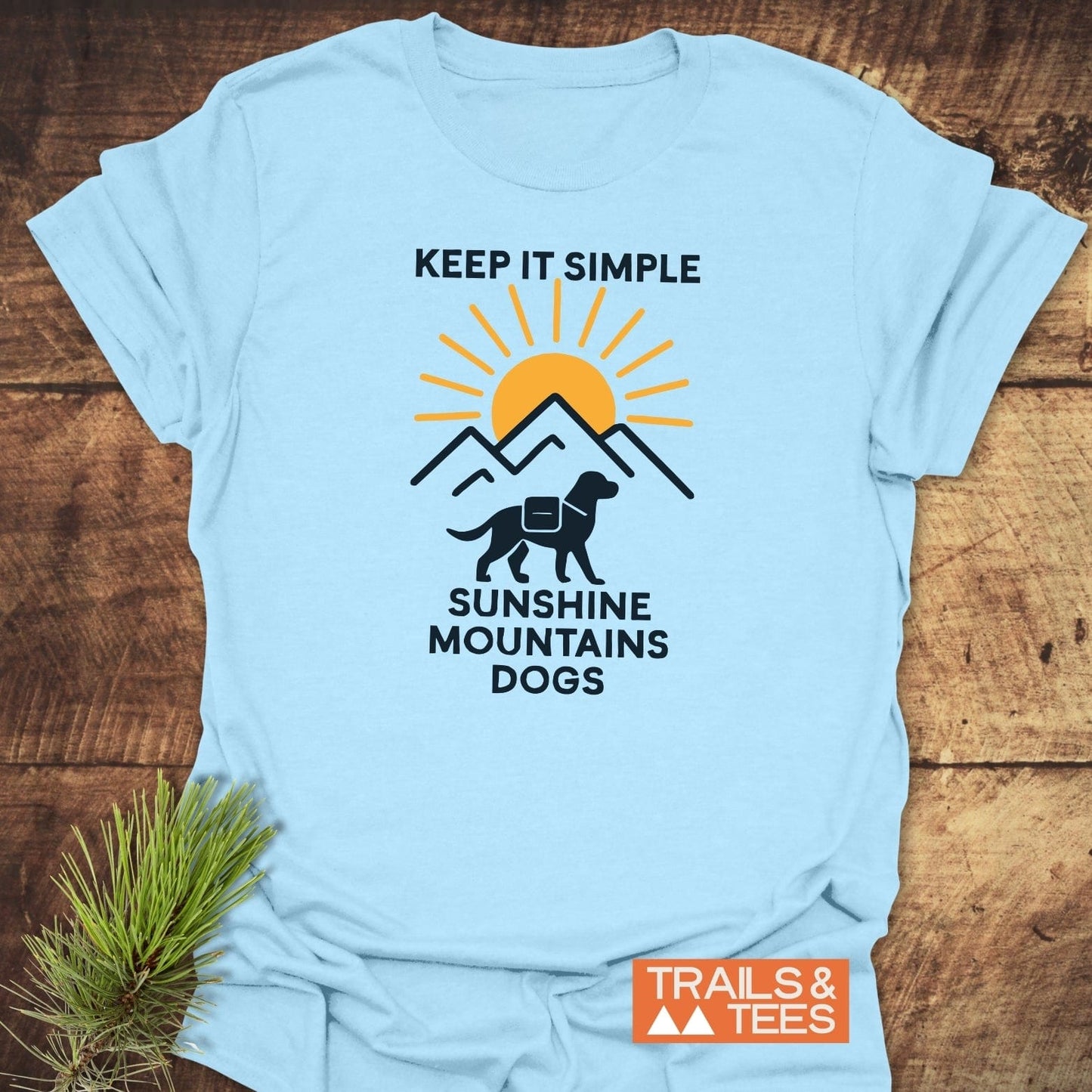 Minimalist Hiking Dog T-Shirt featuring a mountain graphic, sun, and dog silhouette. KEEP IT SIMPLE and SUNSHINE MOUNTAINS DOGS text, branded TRAILS & TEES.