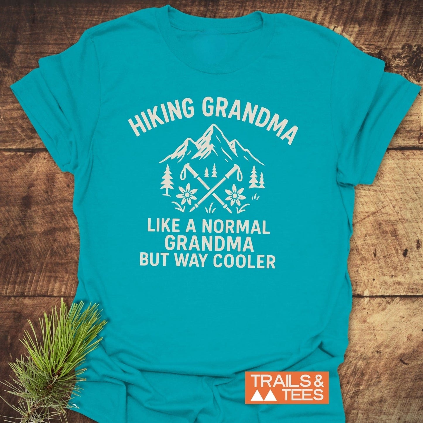 Hiking Grandma Mountain T-Shirt with a mountain peak graphic, hiking poles, and alpine flowers. Made from soft cotton, designed for comfort and outdoor adventures.