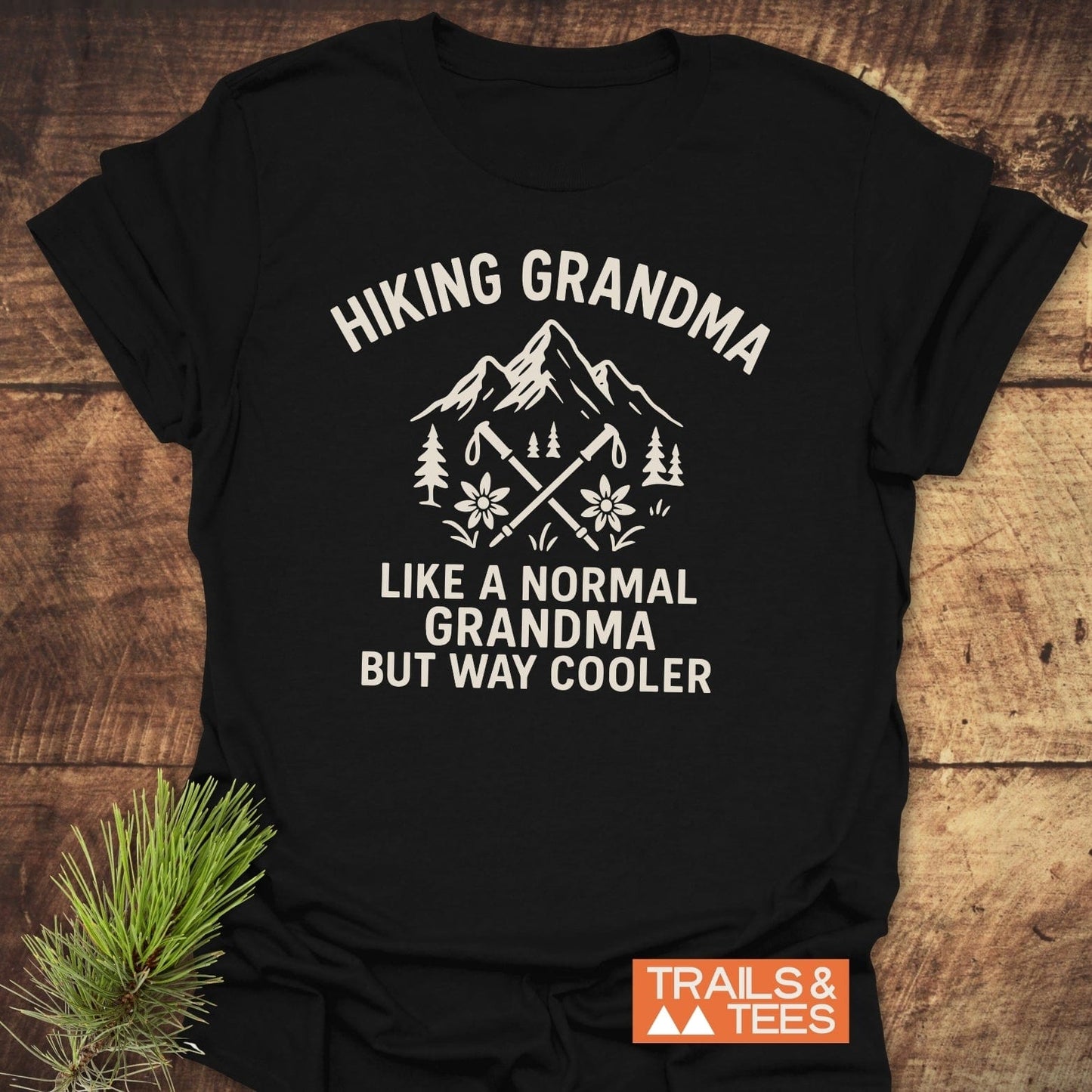 Hiking Grandma Mountain T-Shirt on wood, featuring mountain, hiking poles, trees, flowers graphic. Soft cotton, durable print, perfect for outdoor-loving grandmothers.