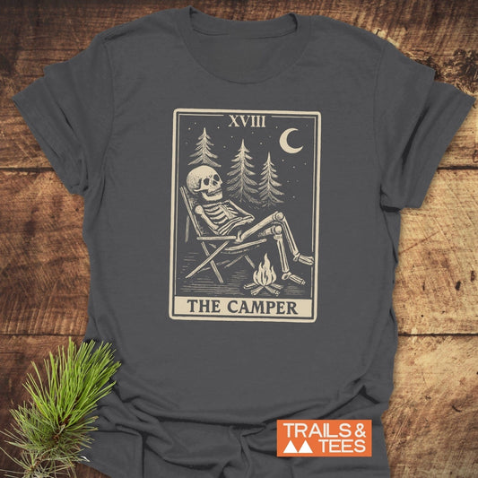 The Camper Tarot T-Shirt features a skeleton lounging by a campfire under a starry sky, symbolizing outdoor adventures. Includes XVIII and THE CAMPER text.