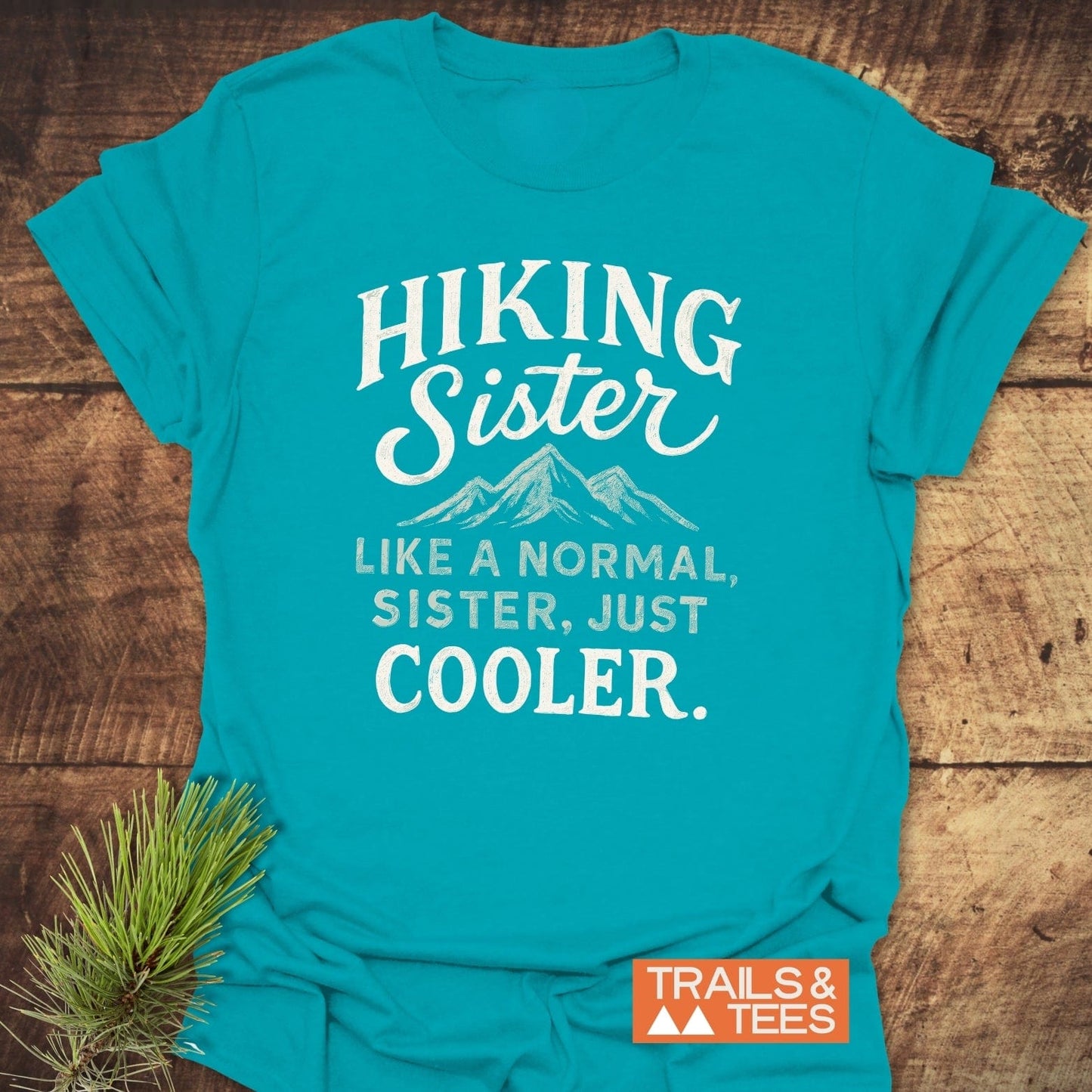 Turquoise Hiking Sister T-Shirt with mountain graphic and text, featuring soft cotton, pre-shrunk fit, and durable print. Logo and pine sprig visible.