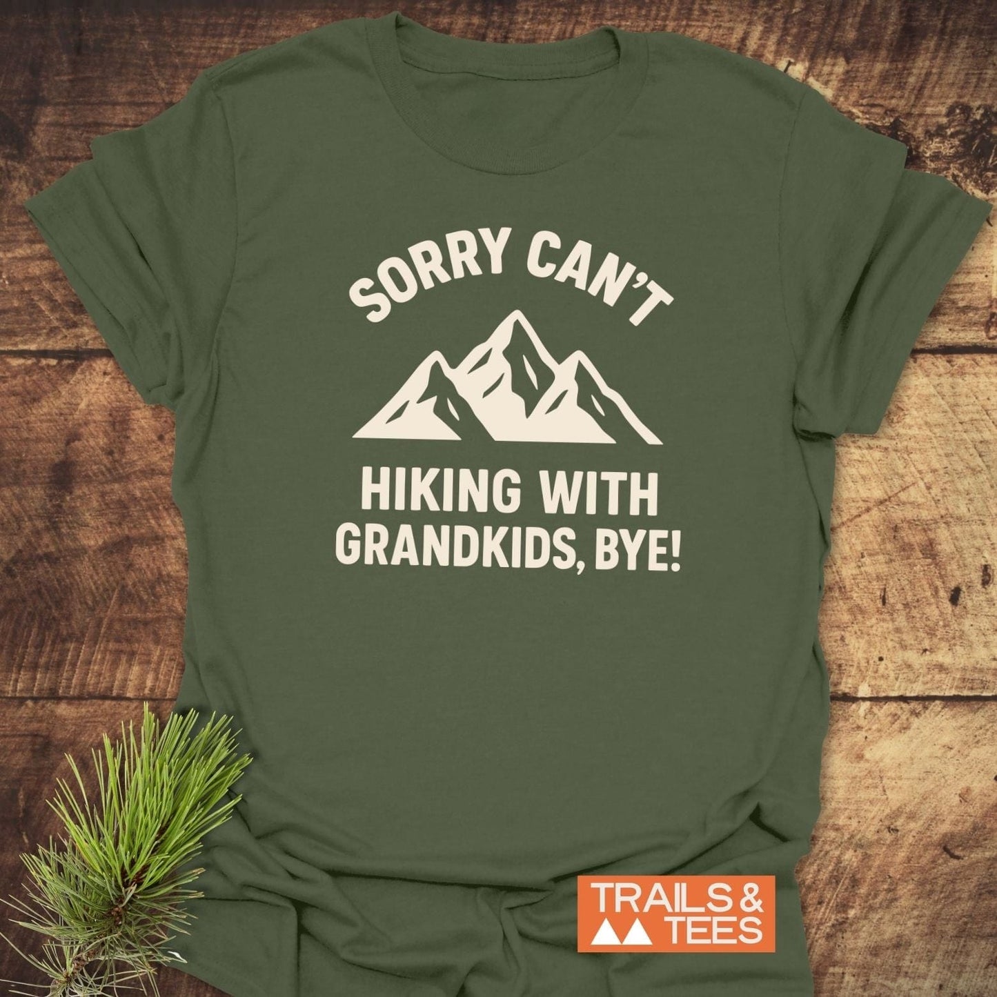 Sorry Hiking With Grandkids T-Shirt on wooden surface, featuring a mountain graphic and phrase, emphasizing comfort, durability, and eco-friendly production by Trails & Tees.