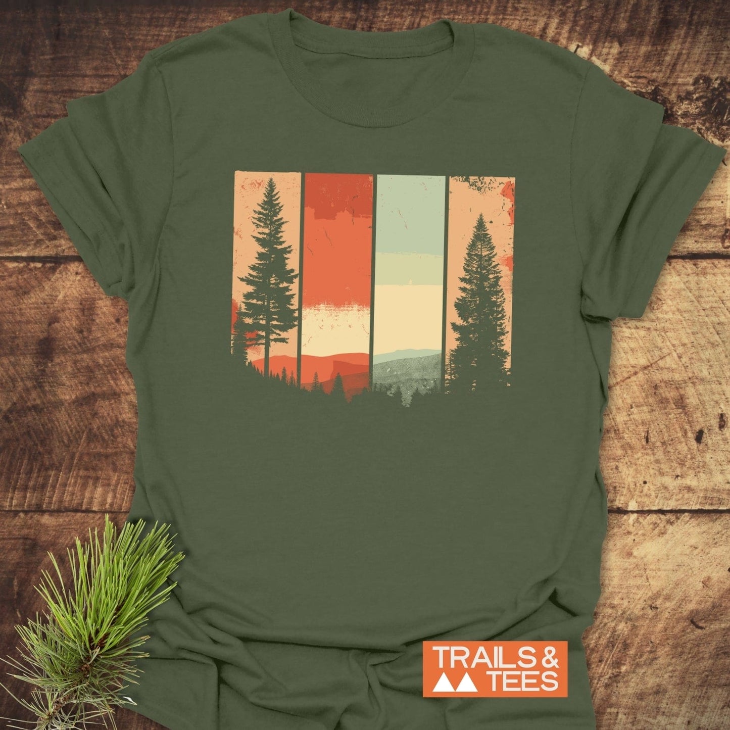 Striped Mountains Retro T-Shirt with vintage forest graphic on olive-green cotton, laid flat. Features durable prints and TRAILS & TEES logo for outdoor enthusiasts.