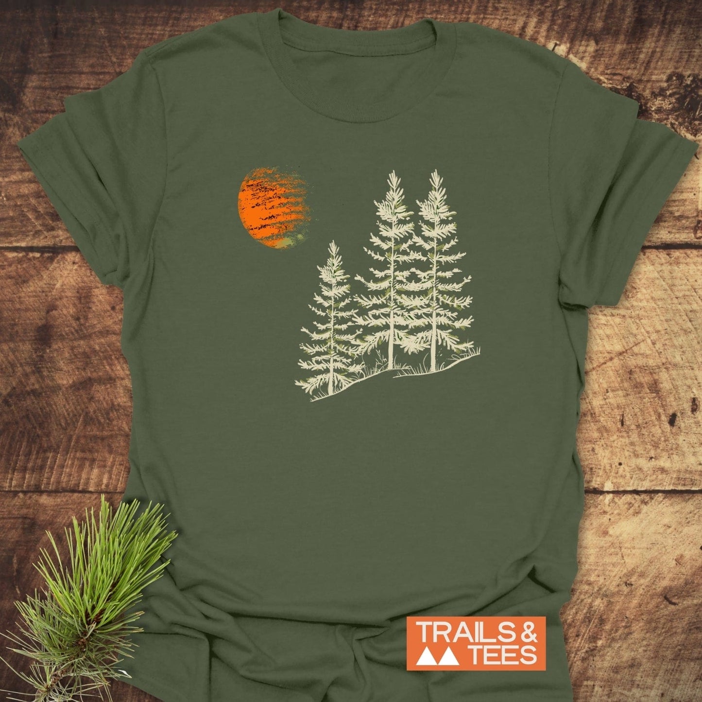 Forest And Moon T-Shirt featuring a nature graphic of pine trees and an orange sun on a rustic wooden surface, highlighting its outdoor-inspired design.