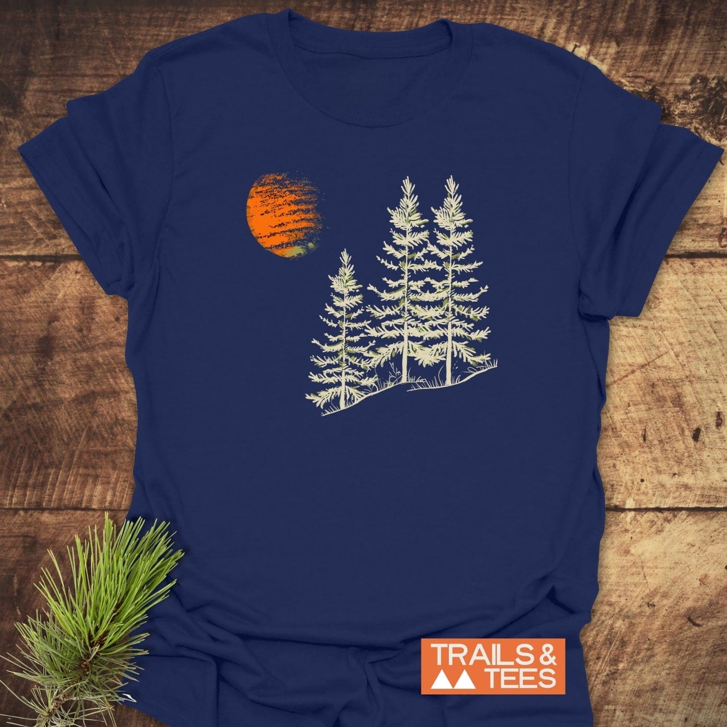 Forest And Moon T-Shirt: Navy blue tee with a graphic of three pine trees and an orange sun, showcasing outdoor-inspired design.