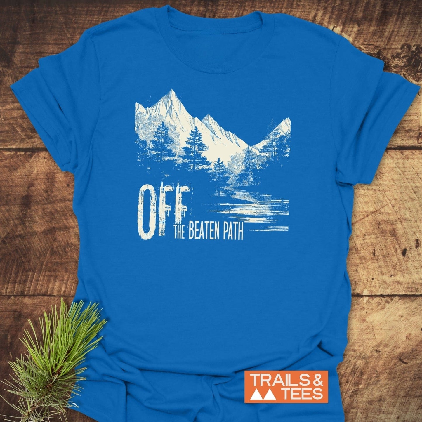Off The Beaten Path T-Shirt featuring a mountain design, crafted from soft cotton with durable prints. Includes Trails & Tees logo, perfect for outdoor enthusiasts.