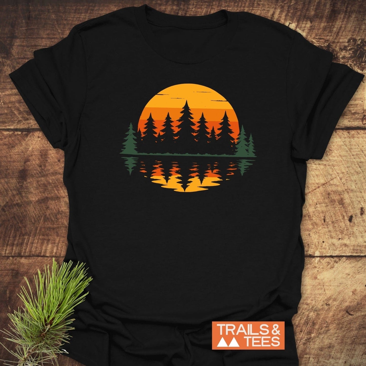Retro Sunset Pines T-Shirt on a wooden surface, featuring a pine-tree silhouette against a sunset. Made from soft, lightweight cotton for comfortable, everyday outdoor adventures.