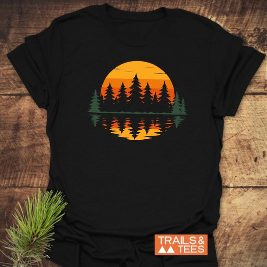 Retro Sunset Pines T-Shirt on a wooden surface, featuring a pine-tree silhouette against a sunset. Made from soft, lightweight cotton for comfortable, everyday outdoor adventures.