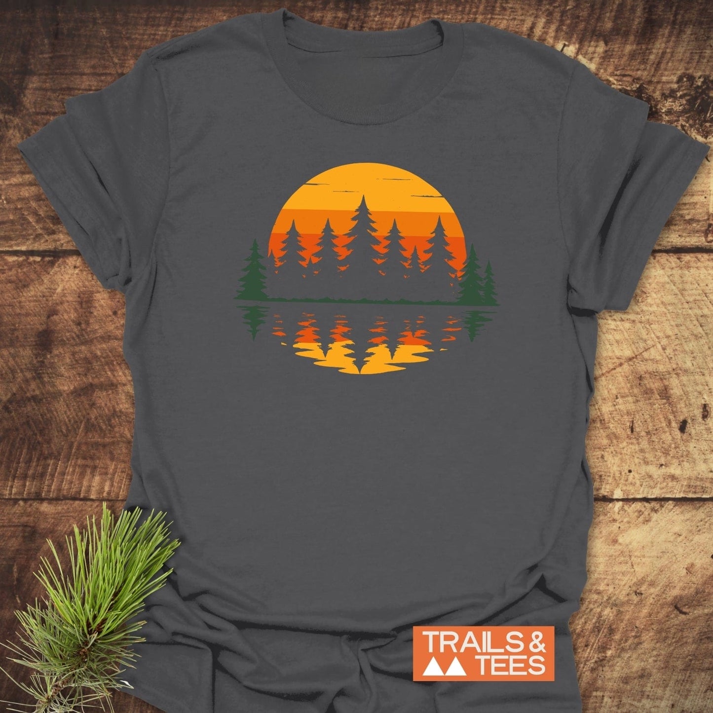 Retro Sunset Pines T-Shirt with an orange-yellow sun and evergreen tree graphic, crafted from ring-spun cotton for comfort and durability, laid flat.