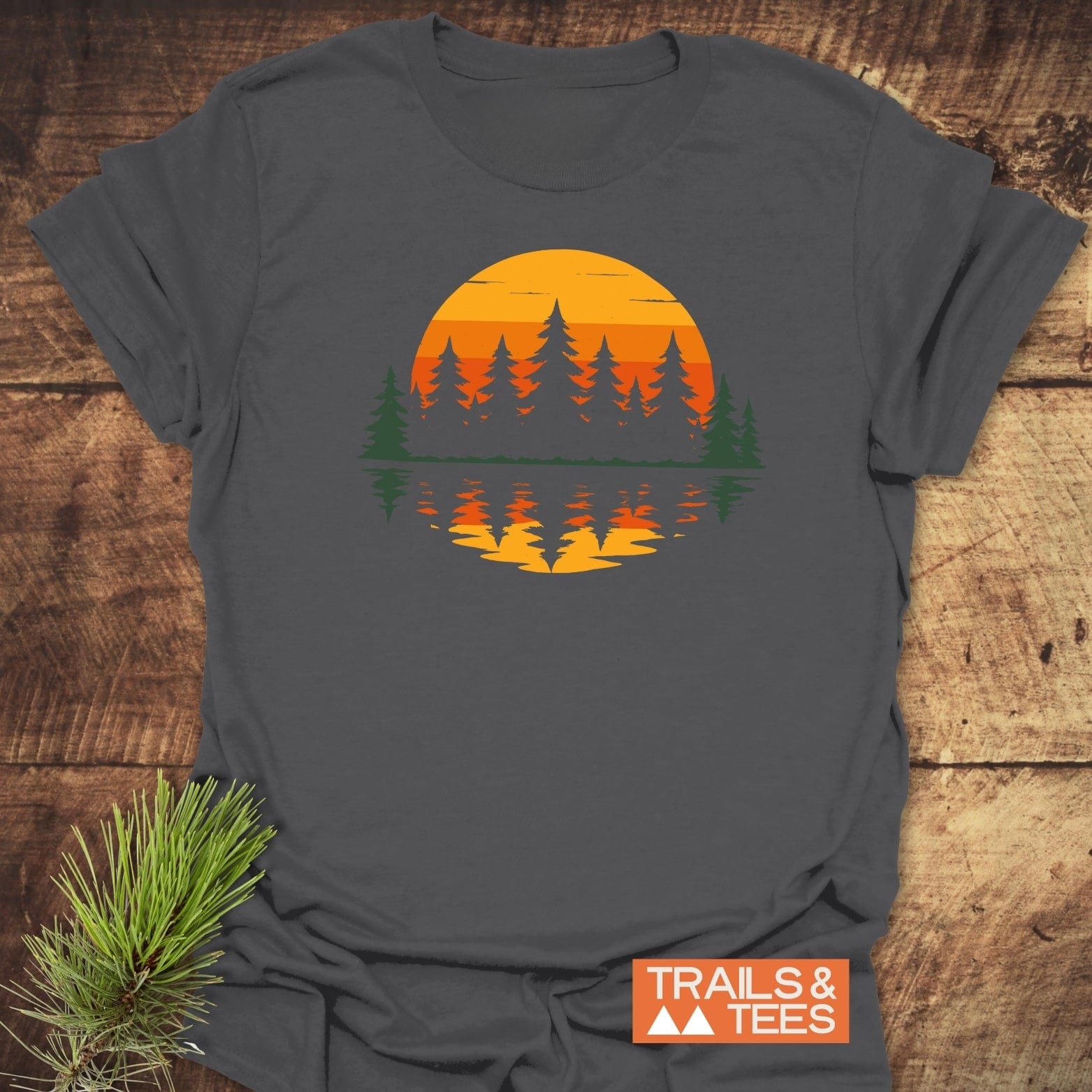 Retro Sunset Pines T-Shirt with an orange-yellow sun and evergreen tree graphic, crafted from ring-spun cotton for comfort and durability, laid flat.
