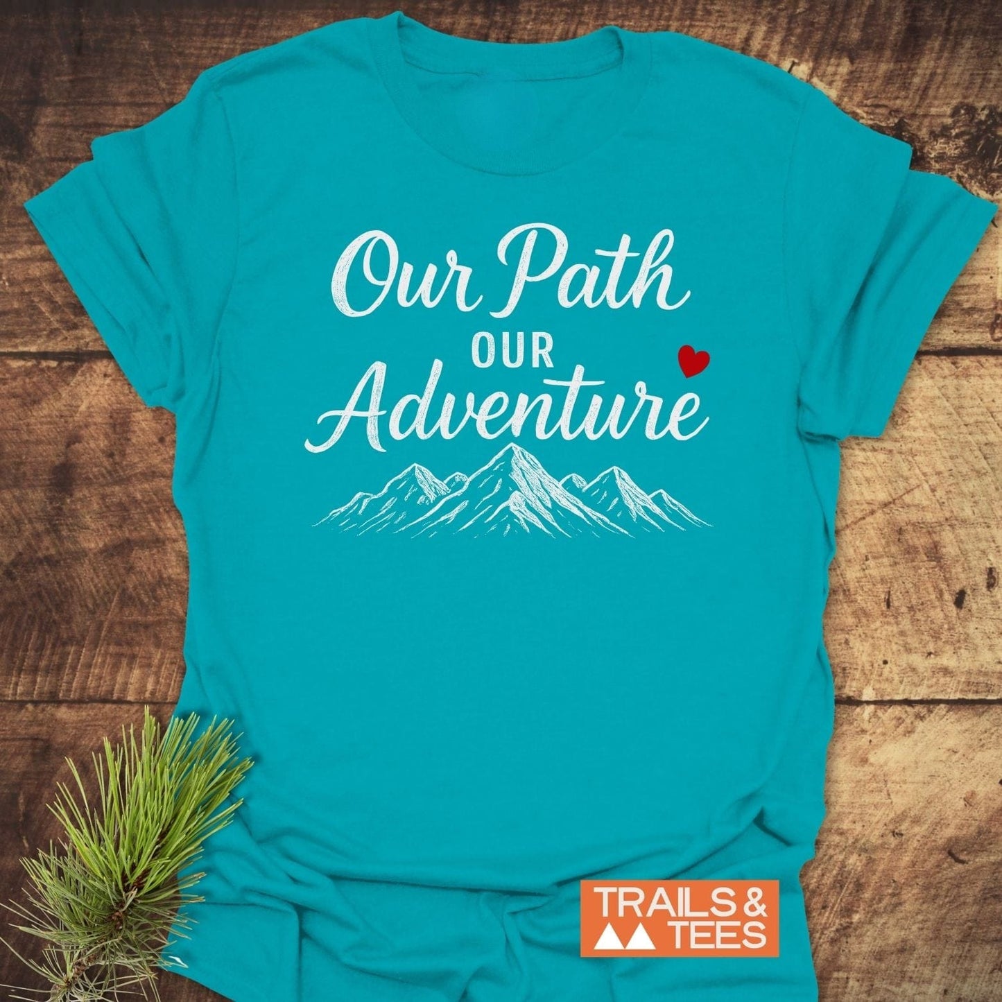Our Path Couple T-Shirt featuring mountain peaks and “Our Path Our Adventure” slogan, styled with pine sprig, embodies trail-tested comfort and timeless outdoor design.