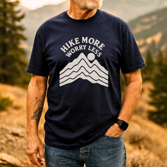 Man wearing Hike More Worry Less T-shirt with mountain graphic and sun, standing outdoors. Soft cotton, pre-shrunk, durable print for outdoor enthusiasts.