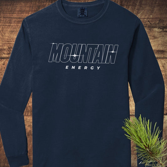 Navy crewneck Mountain Energy Comfort Colors Longsleeve Tee with outlined chest lettering, laid on wood surface, featuring pine needle accent.
