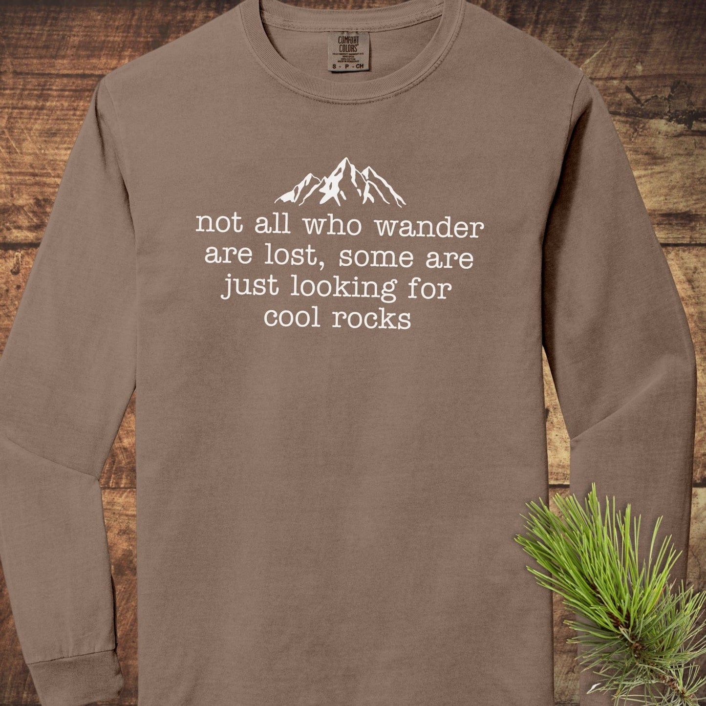 Looking For Cool Rocks Comfort Colors Long-Sleeve Tee with mountain graphic and slogan, laid flat on wood. Made of 100% ring-spun cotton for softness.