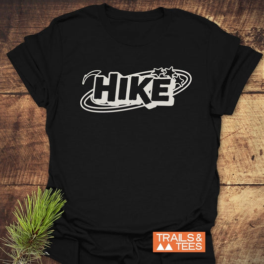 Black Hike Graphic T-Shirt on wooden surface with bold white HIKE and stars, featuring Trails & Tees logo; crafted for comfort and outdoor adventures.