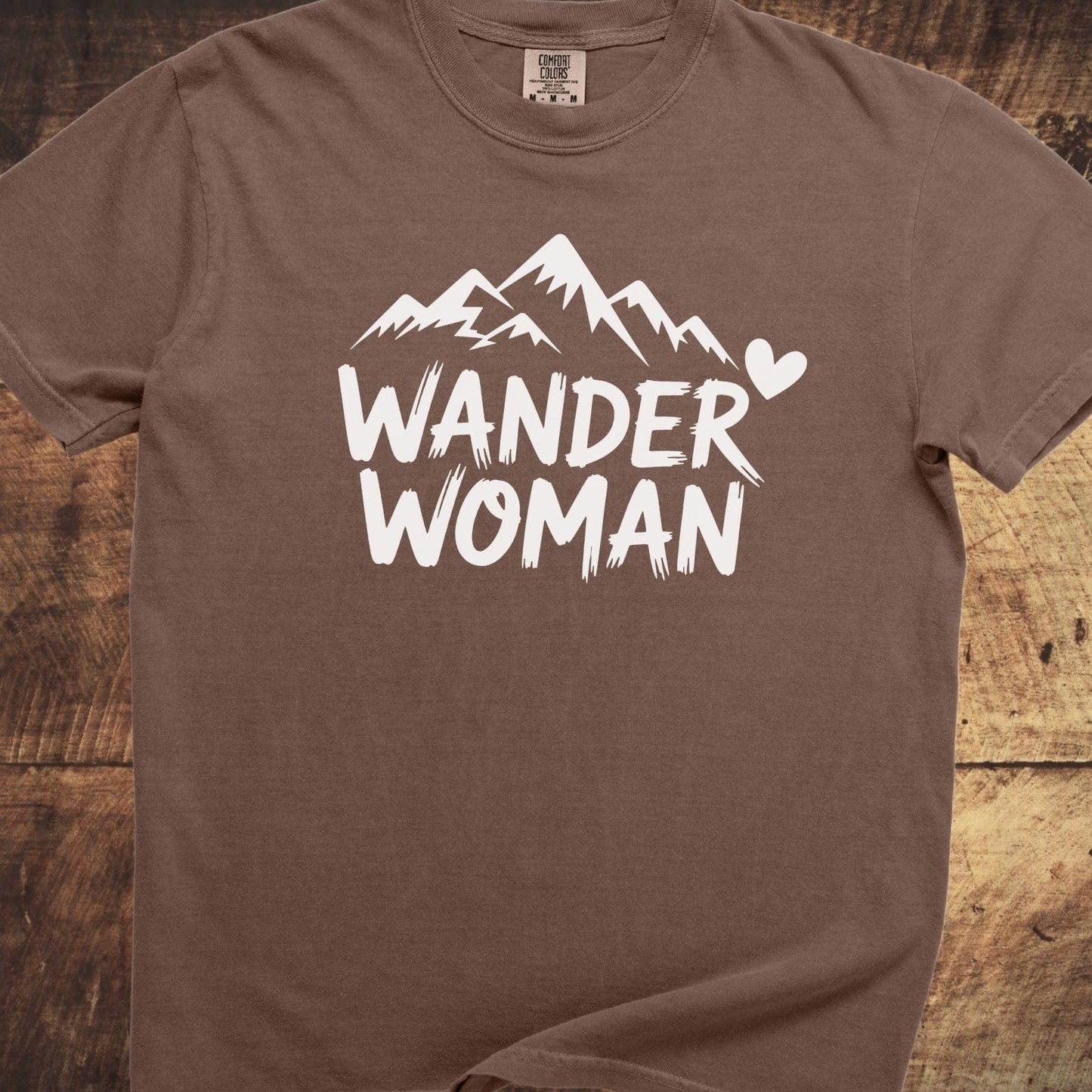 Wander Woman Comfort Colors 1717 Tee: Brown graphic tee with a white mountain design and WANDER WOMAN text, offering a relaxed fit and durable stitching.
