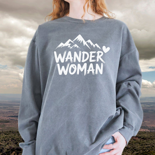 Person wearing the Wander Woman sweatshirt featuring a mountain graphic and heart. Oversized fit, slate-gray, made with ring-spun cotton and polyester blend.