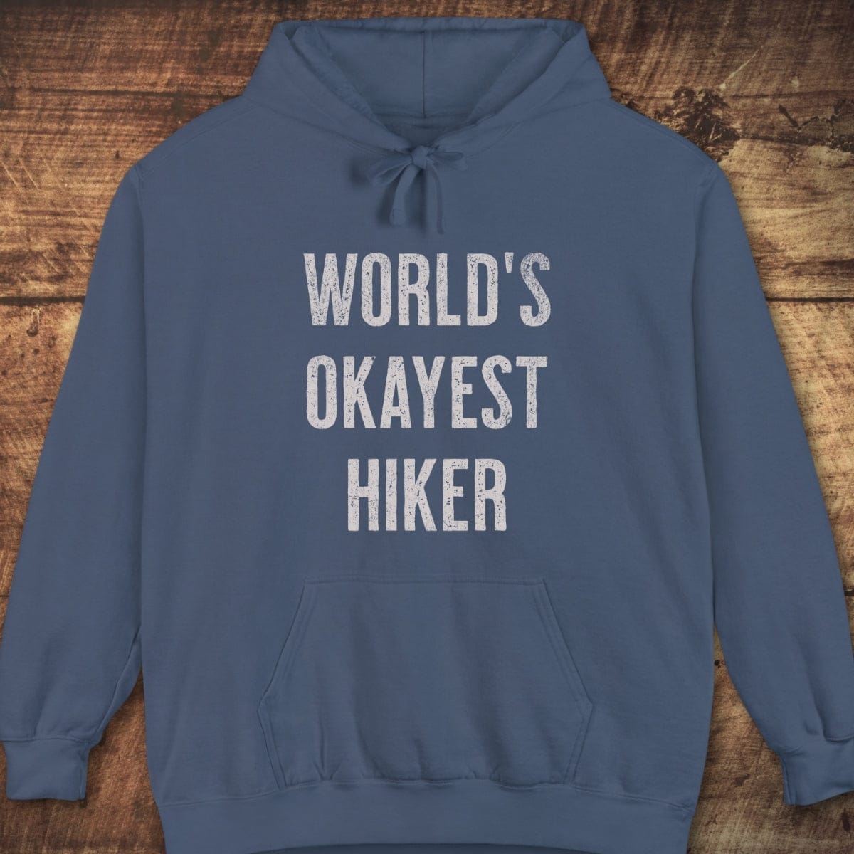 Slate-blue World's Okayest Hiker hoodie with distressed white text, unisex fit, jersey-lined hood, front pouch pocket; garment-dyed for a vintage look.