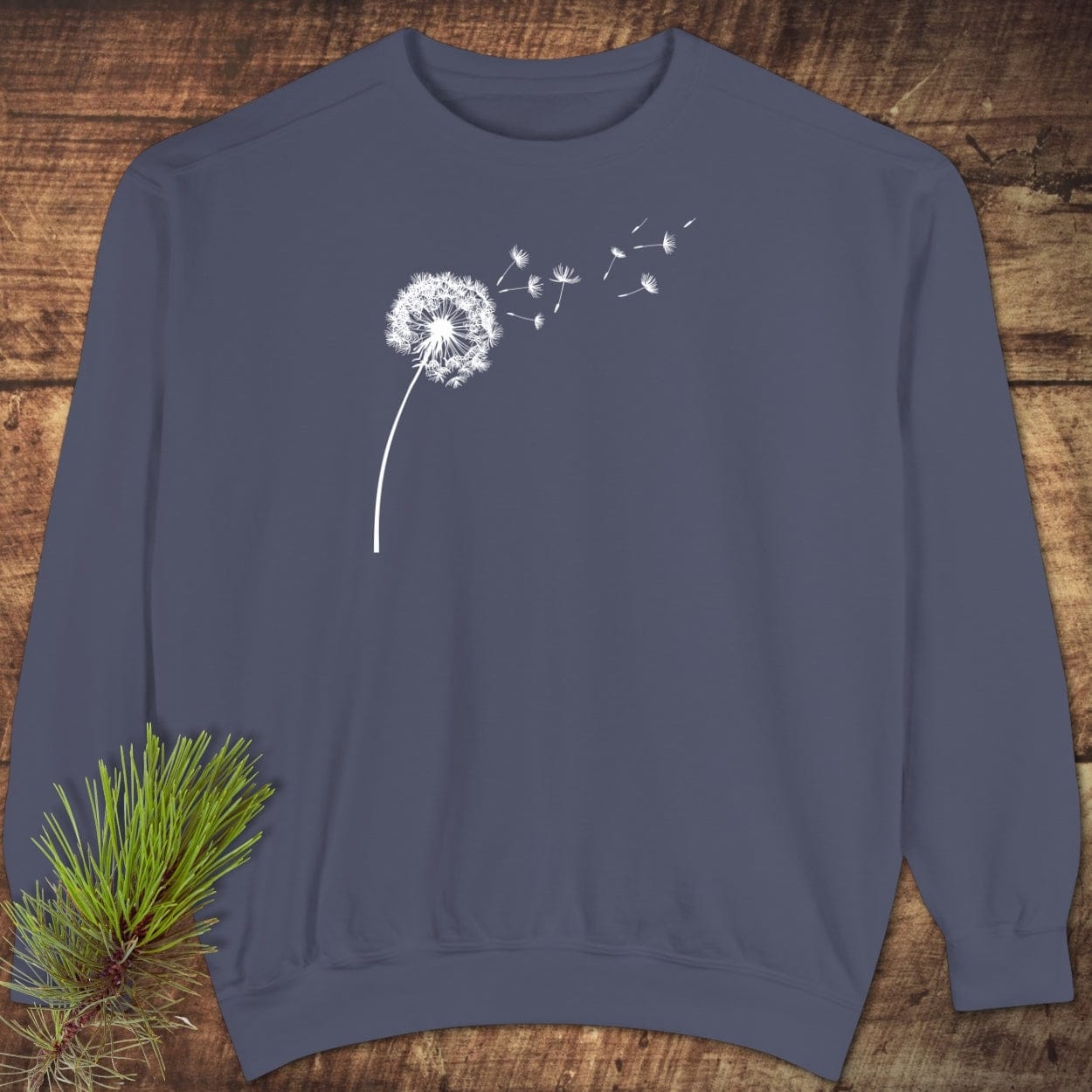 Dandelion Comfort Colors Sweatshirt in slate blue with a white dandelion graphic, displayed on wood. Features a relaxed fit, ring-spun cotton blend, and garment-dyed fabric.