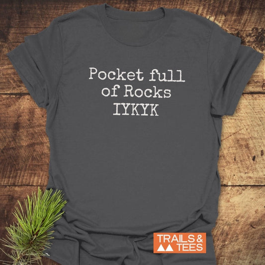 Charcoal-gray T-shirt with Pocket Full Of Rocks IYKYK in white lettering, orange Trails & Tees logo, pine sprig tucked under.