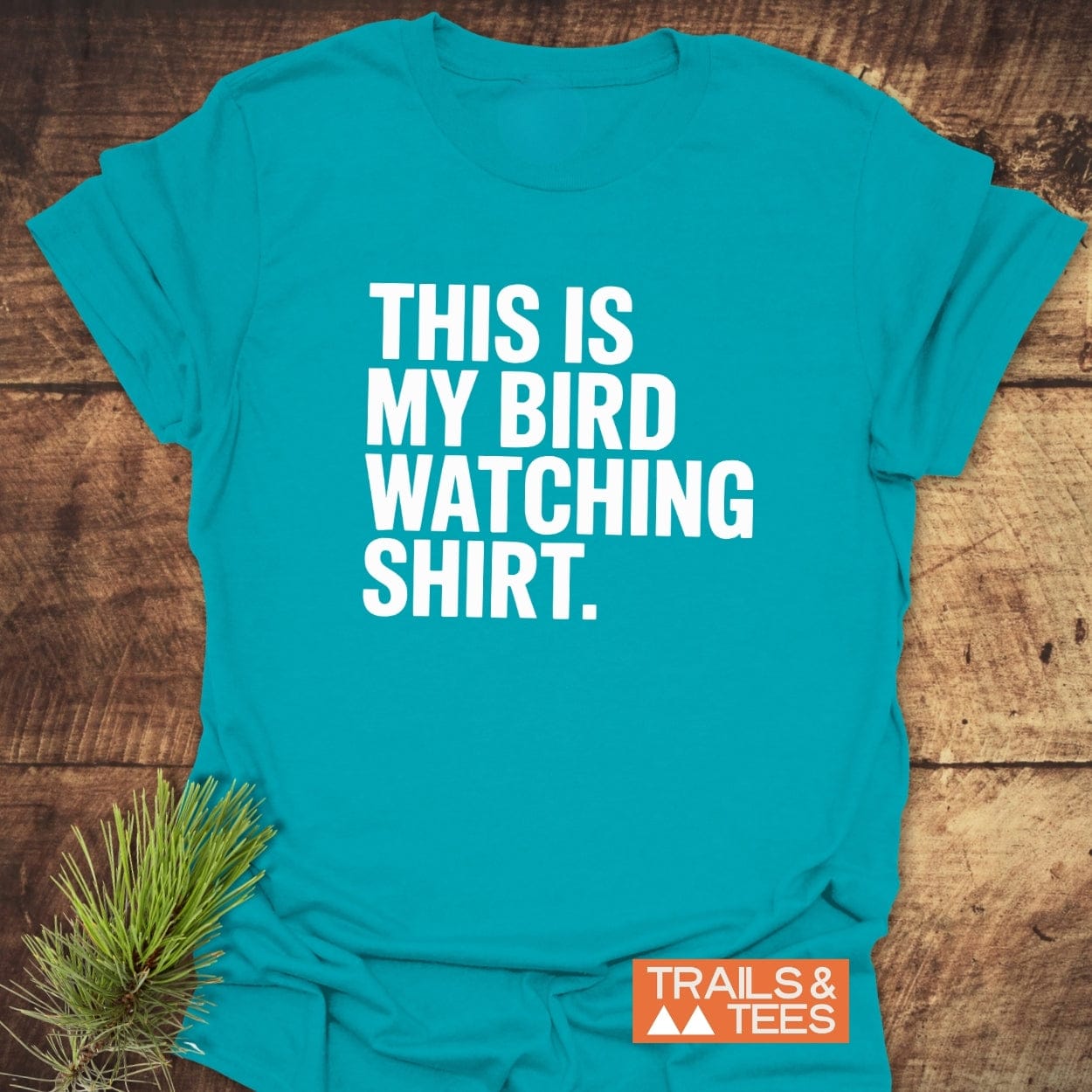Bird Watching T-Shirt in teal with bold white letters, “THIS IS MY BIRD WATCHING SHIRT.” Features “TRAILS & TEES” logo and evergreen sprig for styling.