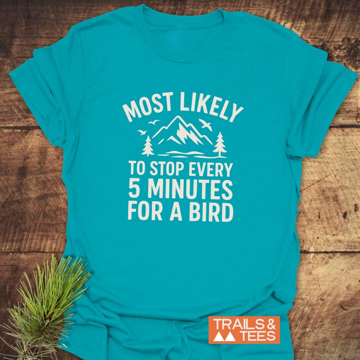 Most Likely Bird Watcher T-Shirt: teal-blue, white print with mountains, trees, birds. Soft ring-spun cotton, pre-shrunk, durable print, and sustainable production.