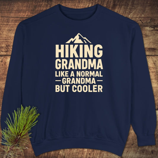 Navy-blue Hiking Grandma Comfort Colors Sweatshirt with cream mountain graphic and text, laid flat on wood, showcasing its relaxed fit and quality fabric.