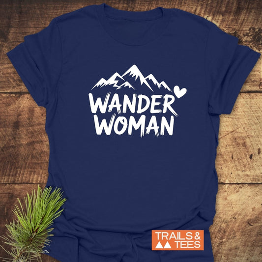 Wander Woman T-Shirt featuring mountain peaks and heart graphic, crafted from soft cotton for comfort, with a rustic pine accent beside it.