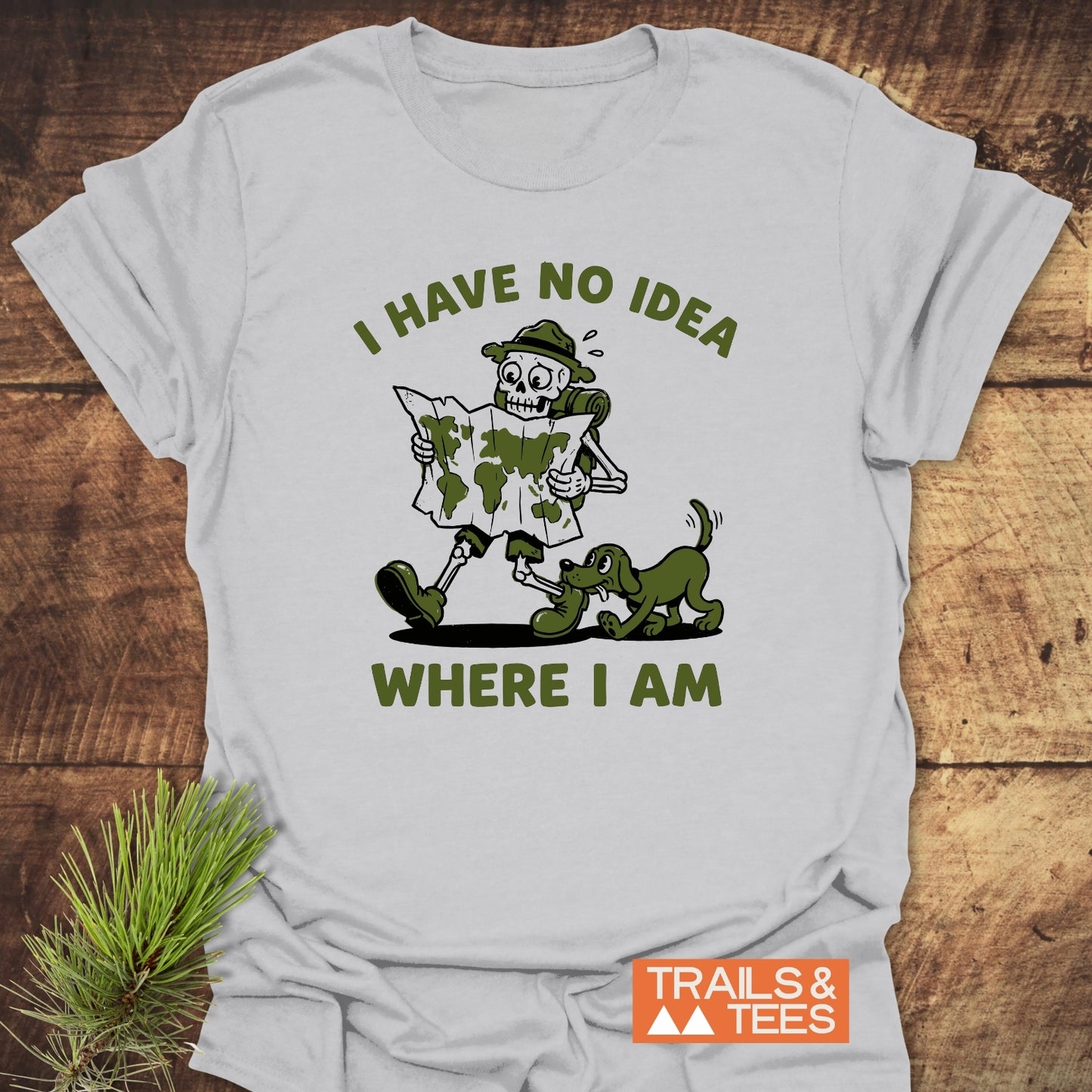 Lost Skeleton Hiker T-Shirt featuring a cartoon skeleton in hiking gear with a playful green dog. Bold text reads, “I HAVE NO IDEA WHERE I AM.” Perfect for adventure lovers.