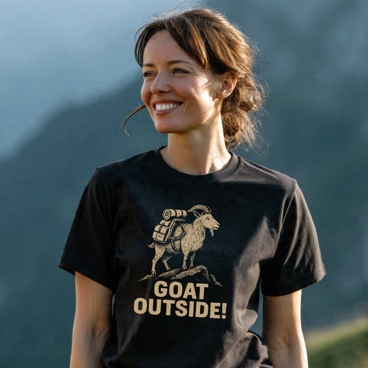 Woman outdoors wearing the Goat Outside! Funny T-Shirt featuring a stylized goat with a backpack. The tee blends comfort and adventure, ideal for outdoor enthusiasts.