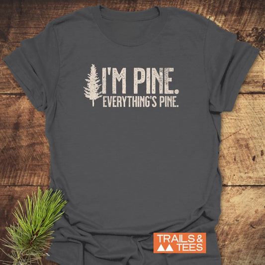 I'm Pine. Everything's Pine. T-Shirt with distressed white pine tree graphic on charcoal-gray, featuring a small pine sprig and 'TRAILS & TEES' logo, showcasing outdoor-inspired comfort and durability.