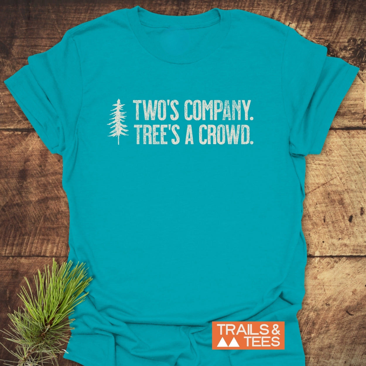 Two's Company Funny T-Shirt featuring a distressed pine-tree graphic and slogan, “TWO’S COMPANY. TREE’S A CROWD.” Crafted from soft cotton, it’s ideal for outdoor enthusiasts.