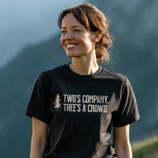 Woman outdoors in a Hike It Out T-Shirt showcasing a pine-tree icon and witty slogan. The shirt embodies comfort and adventure, ideal for nature lovers.