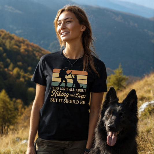 Young woman in a black Hiking And Dogs T-Shirt with retro high-five print, standing next to a large dog in a scenic, hilly autumn landscape, showcasing the shirt's adventurous spirit.