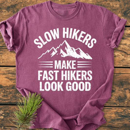 Slow Hikers - Vintage Wash Tee, a plum-colored shirt with a mountain graphic and slogan, folded on wood. Features soft, garment-dyed cotton and relaxed fit. Pine sprig accentuates the natural theme.