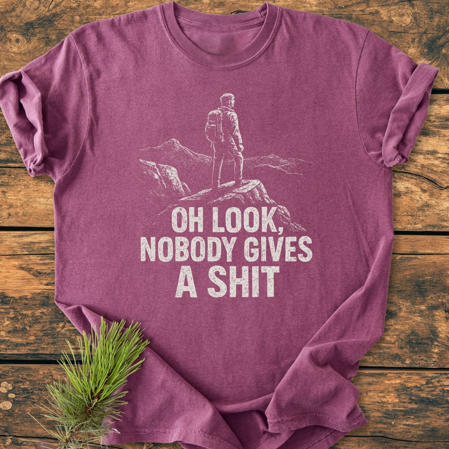 Oh Look - Vintage Wash Tee features a white silhouette of a hiker on a heather-purple garment-dyed shirt, laid flat with a pine sprig, highlighting its relaxed fit and durable double-needle stitching.