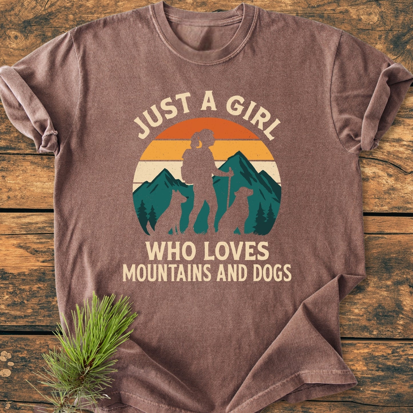 Mountains And Dogs - Vintage Wash Tee featuring retro sunset and hiker graphic with dogs, laid on wood. Made of soft, pre-shrunk 100% ring-spun cotton, offering a relaxed fit and durability.