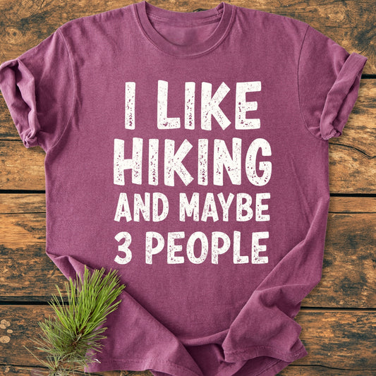 Folded I Like Hiking And Maybe 3 People - Vintage Wash Tee on rustic wood, featuring distressed white slogan, styled with a pine branch. Made from soft, garment-dyed, 100% ring-spun cotton for comfort.