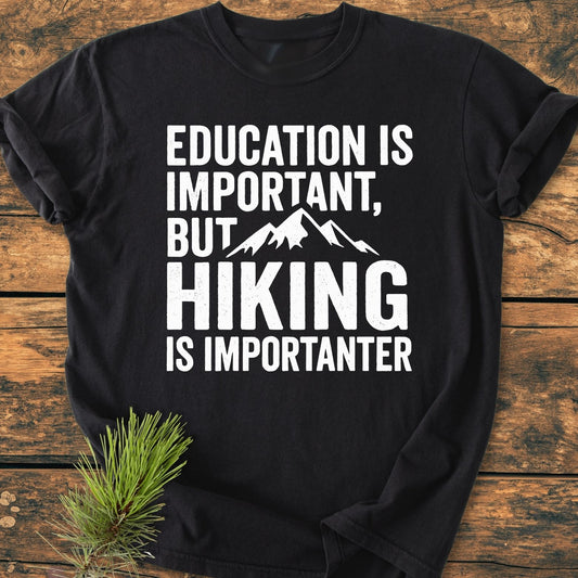 Black Education Is Important - Vintage Wash Tee with white slogan and mountain graphic, styled with a pine sprig on a wooden surface. Relaxed fit, soft-washed, 100% ring-spun cotton.