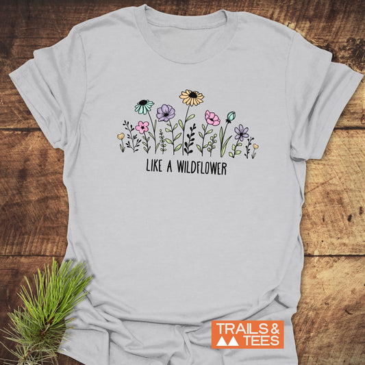 Like A Wildflower T-Shirt featuring pastel wildflowers and “LIKE A WILDFLOWER” text. Crafted from soft, lightweight cotton, it's designed for adventure. Includes the “TRAILS & TEES” logo.
