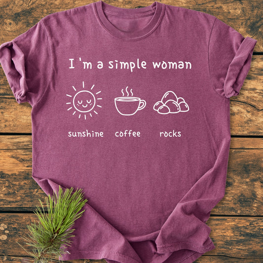 The Sunshine, Coffee, Rocks - Vintage Wash Tee features I'm a simple woman text with sun, coffee cup, and stones icons, showcasing its comfortable, relaxed fit on a wooden surface.