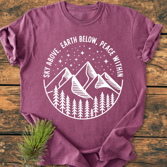 Sky Above - Vintage Wash Tee, featuring a white circular graphic with mountains, pine trees, and stars, laid on wood. The heather-purple tee offers a relaxed fit with durable double-needle stitching.