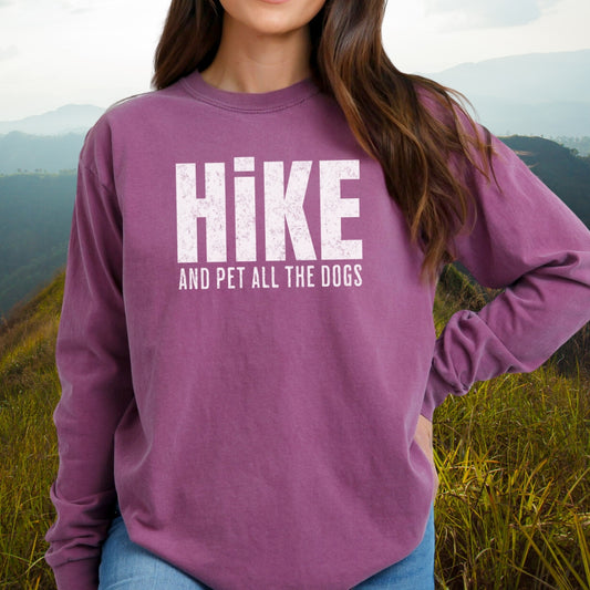 Person outdoors in Hike And Pet Dogs Long-Sleeve Tee, showcasing bold white text on muted purple. Styled for comfort with blue jeans, embodying casual adventure and cozy fit.