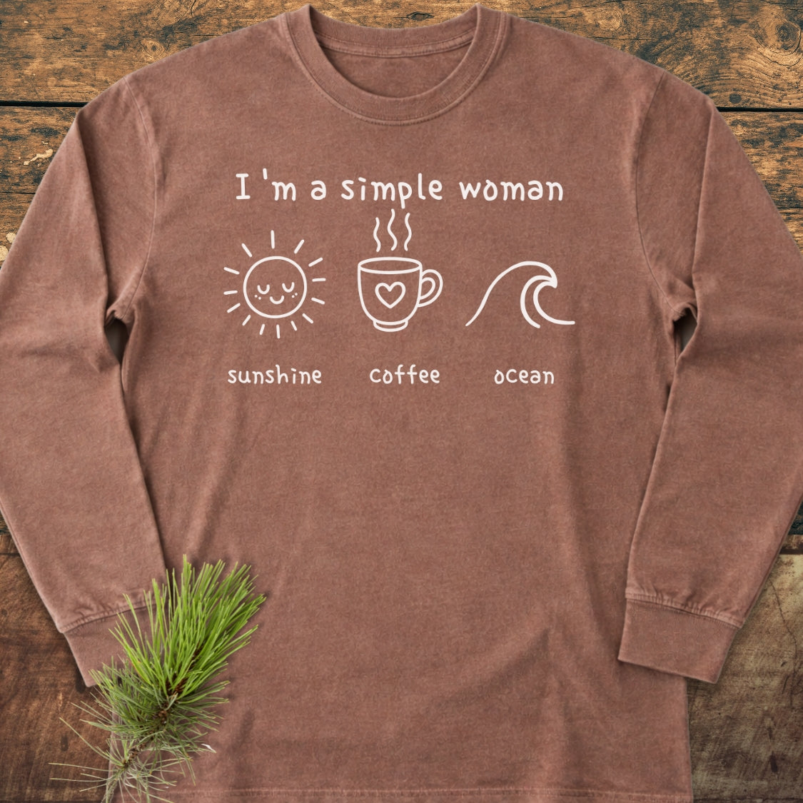 I'm A Simple Woman - Sunshine Coffee Ocean Long-Sleeve Tee, featuring white graphics of a sun, coffee mug, and ocean wave on brown fabric, laid flat with a pine sprig beside it.